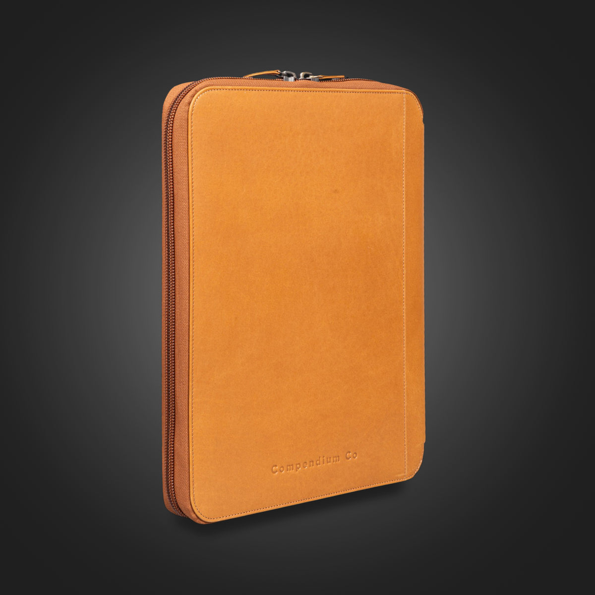 Compendium Co tan leather compendium closed, standing on dark background
