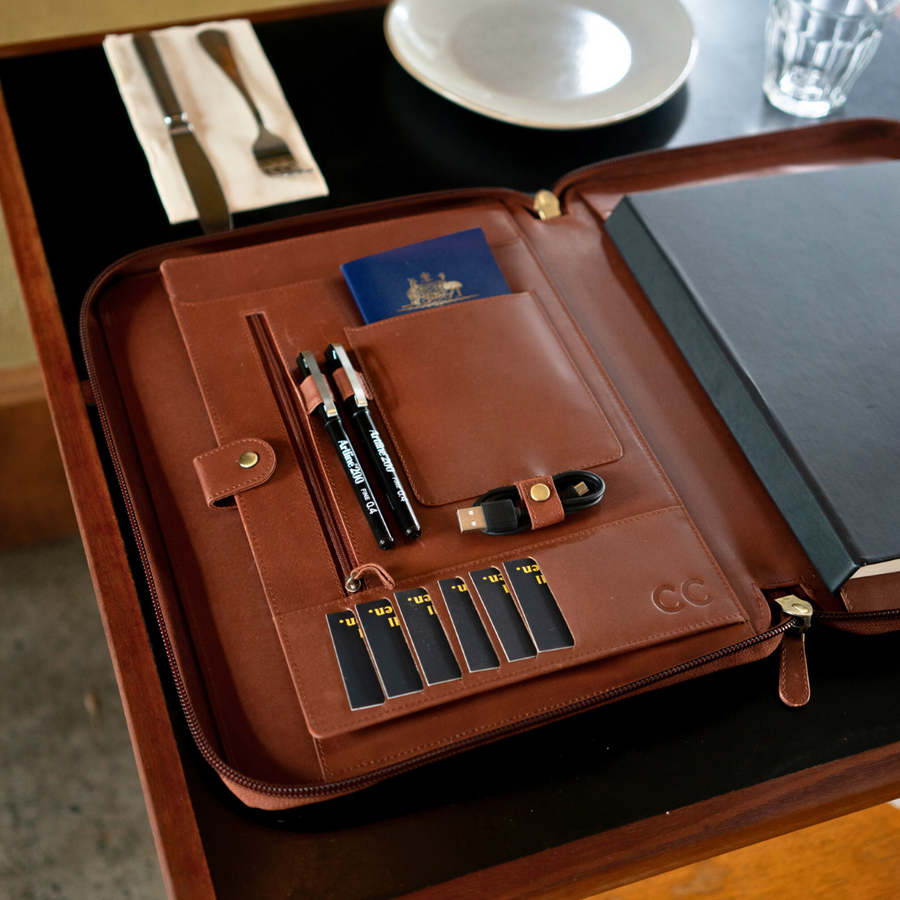 Dark brown leather compendium with passport, pens, and USB drive displayed on a restaurant table.
